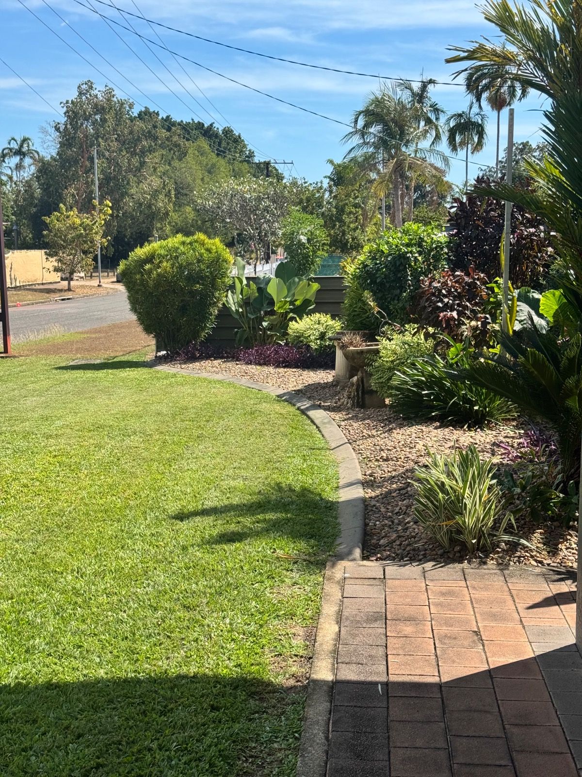 Green manicured lawn bordered by curved garden beds with tropical plants and shrubs under a blue sky in Alawa NT