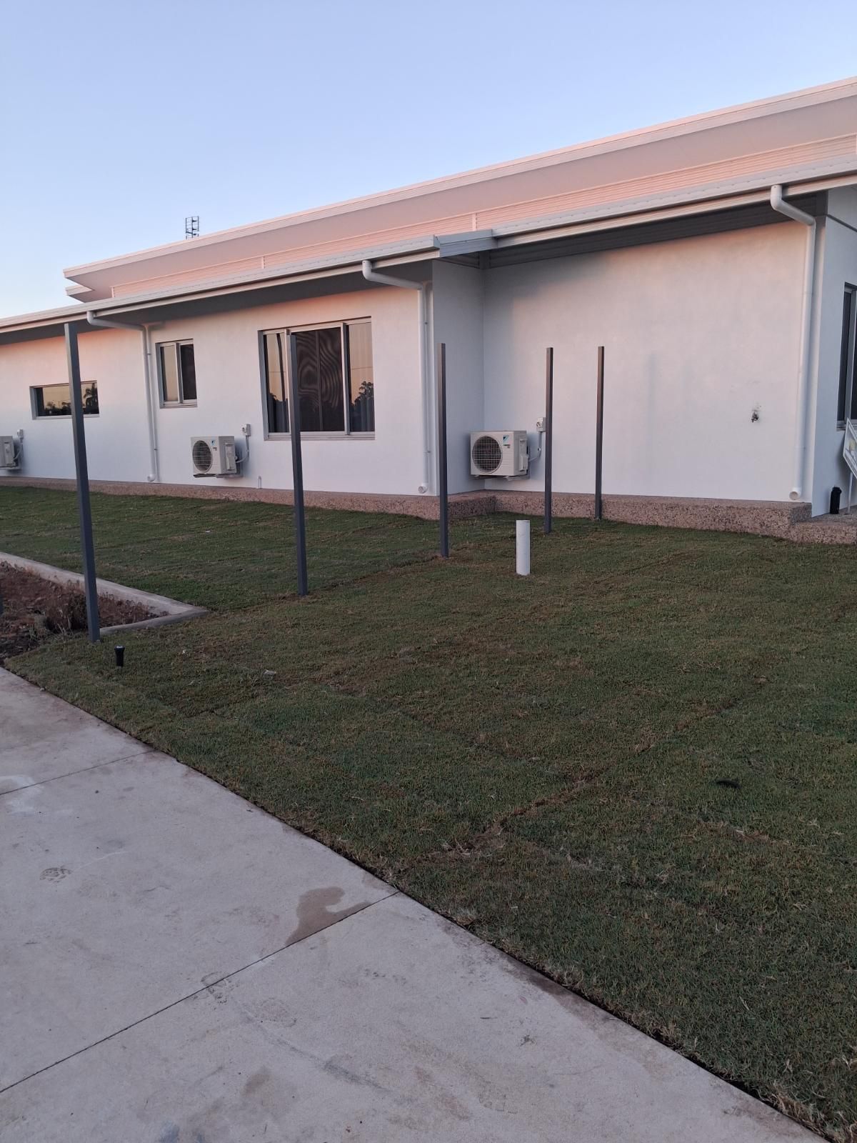 Newly laid green lawn with metal posts next to a white modern house with multiple air conditioners at Marrara Gardens NT.