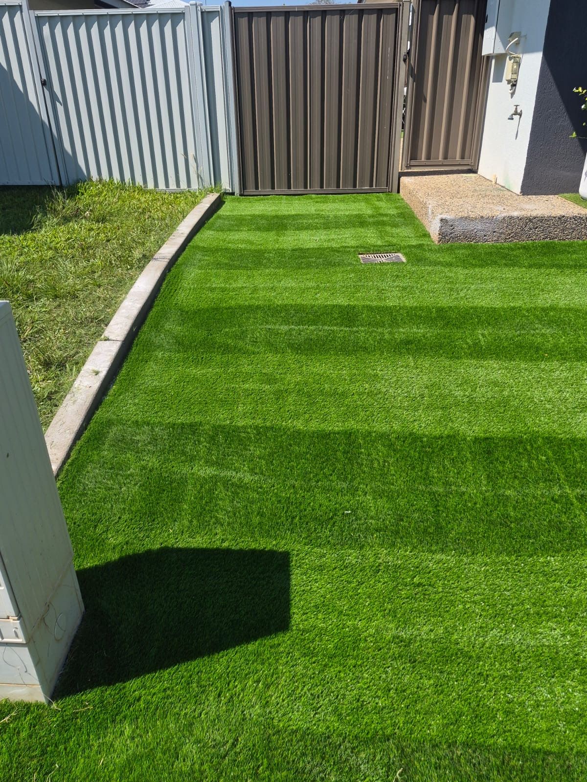 Backyard area with freshly laid artificial grass bordered by a concrete edge and metal fence in Berrimah.